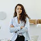 Confident young woman in a light blue blazer with arms crossed, standing in a minimalist office.